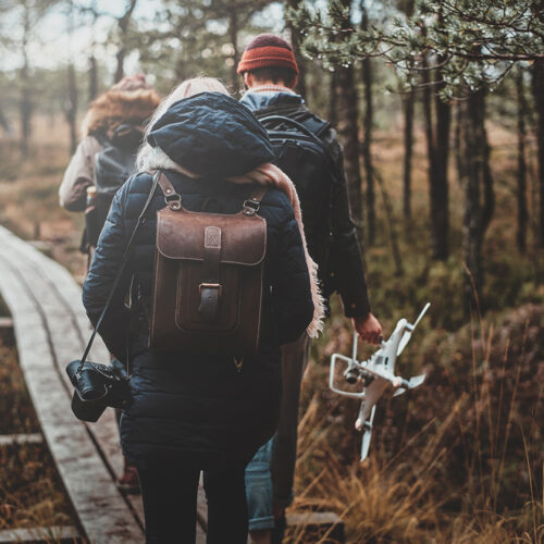 In gloomy autumn day group of friends are hiking in nice park, man is holding a drone.