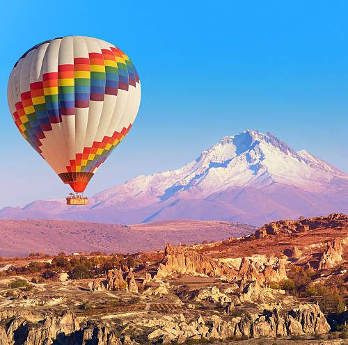 Balloon flying over rock landscape at Cappadocia Turkey with Erciyes Mountain.